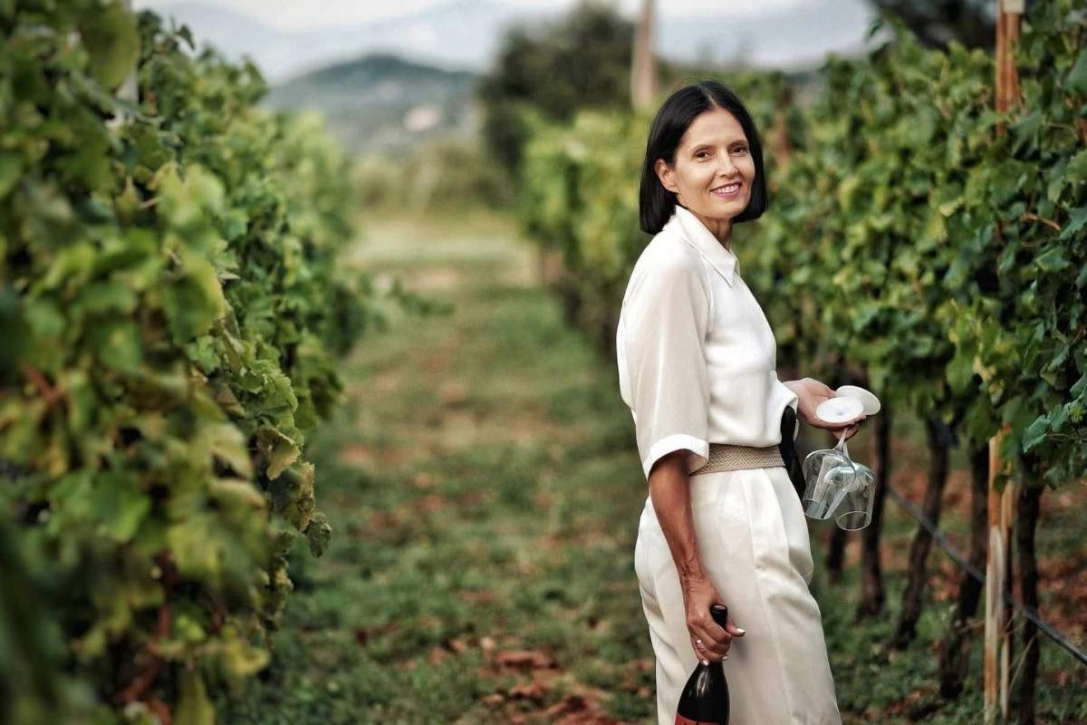 Woman holding glasses and bottle of Cine Wine Vukčević wine among vines